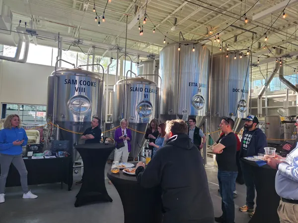 A crowd of members networking among brewery tanks