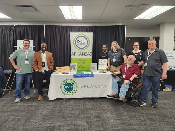 Members gathered at the ISC2 Arkansas chapter table, with the chapter banner behind them