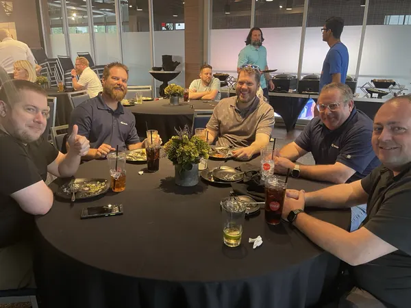 Members seated around a dinner table, one giving a thumbs up